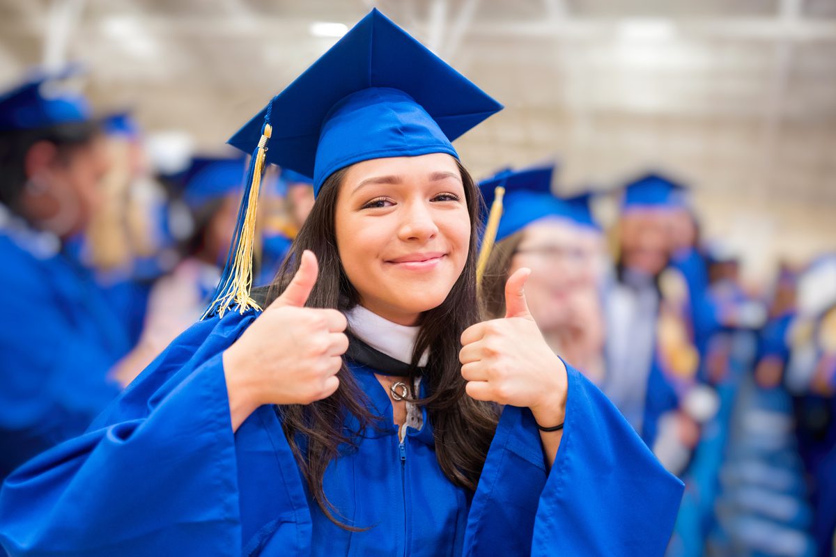 Student in graduation cap and gown giving two thumbs up